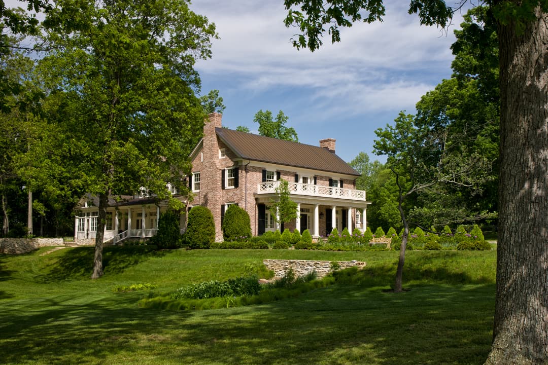 Brick traditional house set on rolling horse farm with classical front porch.